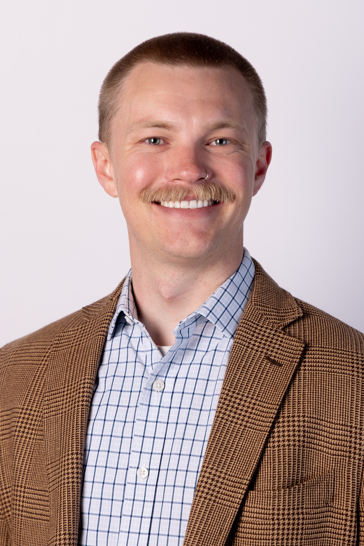 Man with a moustache in a tan checked jacket on a soft backdrop