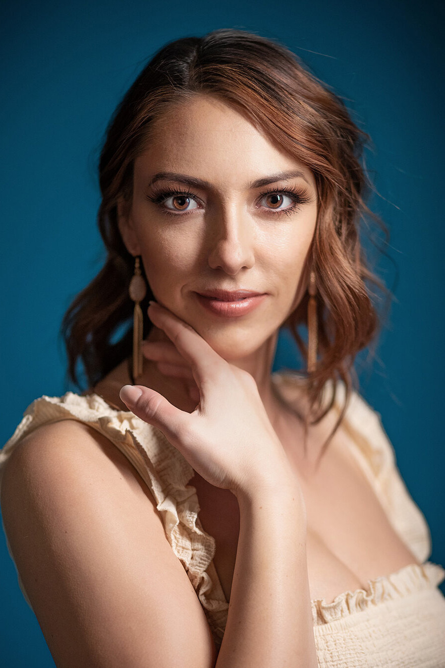 Woman with auburn hair and statement earrings on a teal backdrop