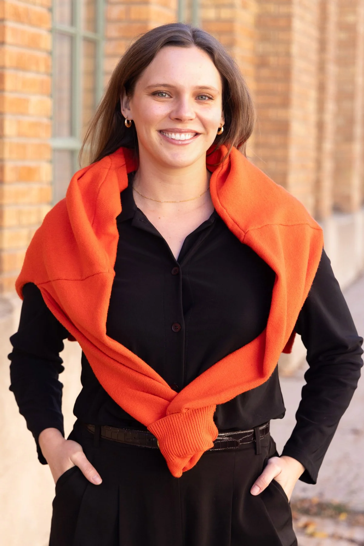 Professional woman in black with an orange sweater draped over her shoulders outside a brick building