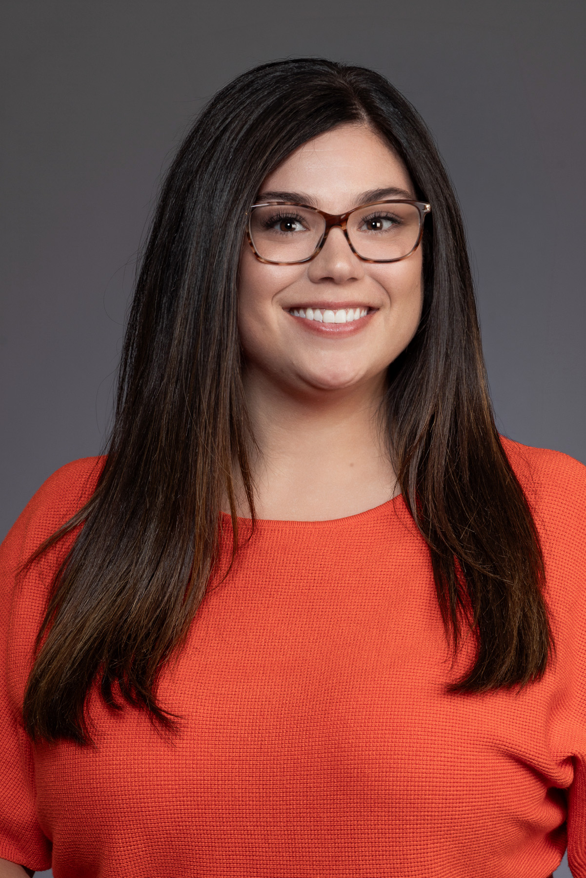 Professional woman with long dark hair, glasses and a coral top