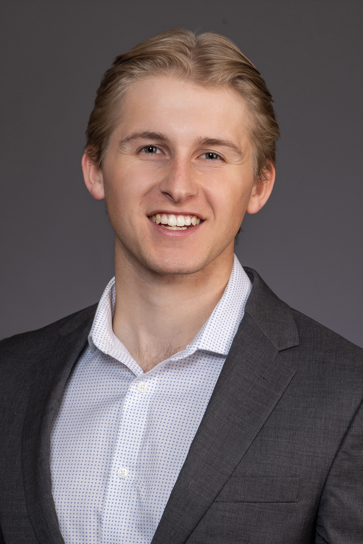 Young professional with blonde hair in a charcoal suit on grey