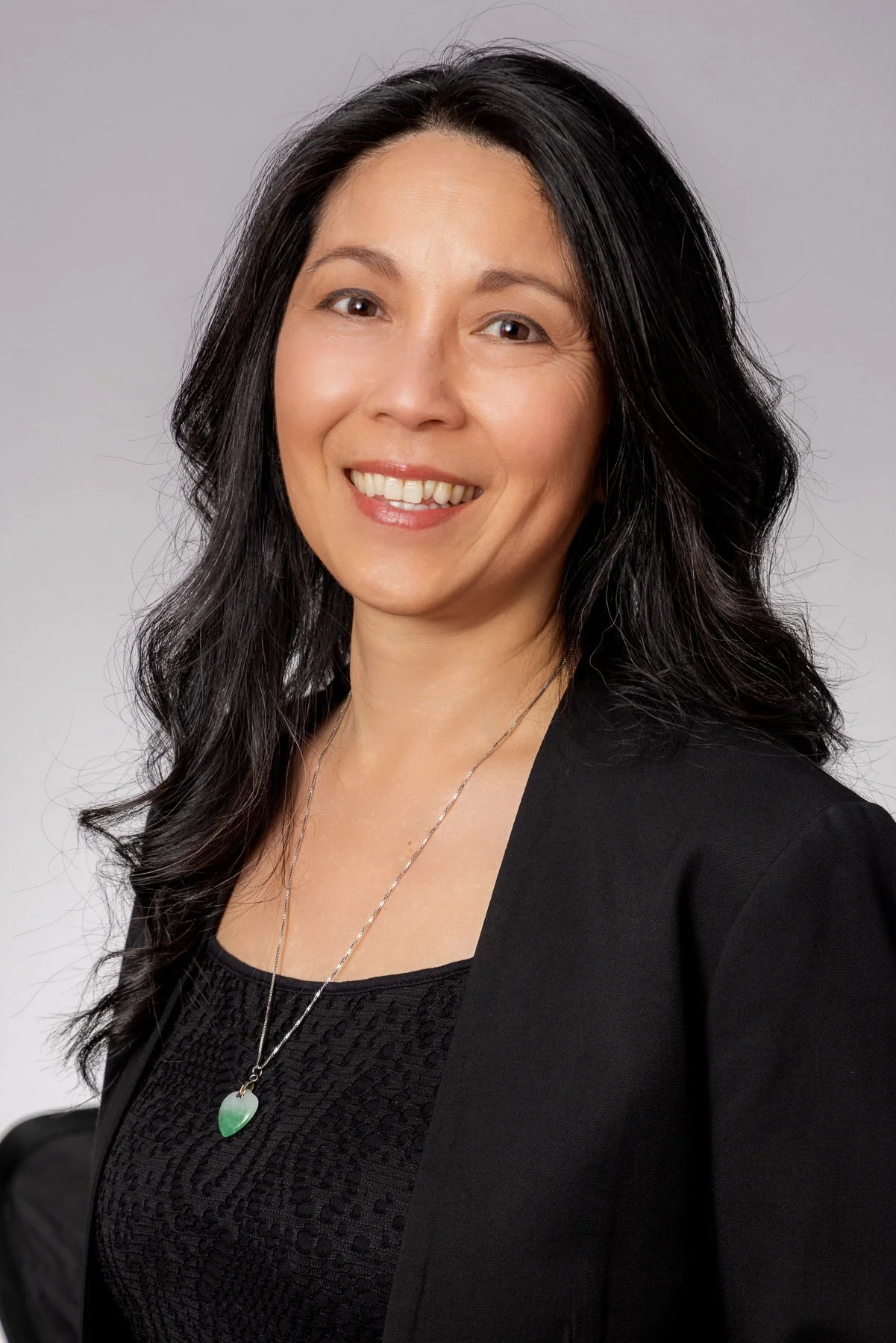 Executive woman with dark wavy hair in a black jacket and jade pendant
