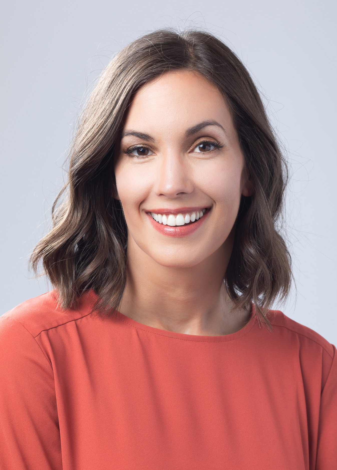 Smiling professional woman in a coral blouse on light grey