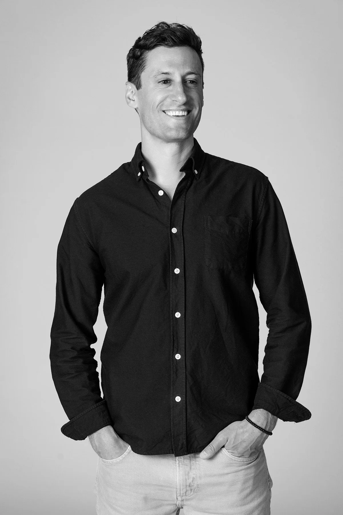 Black and white portrait of a man in a black button-down with hands in pockets