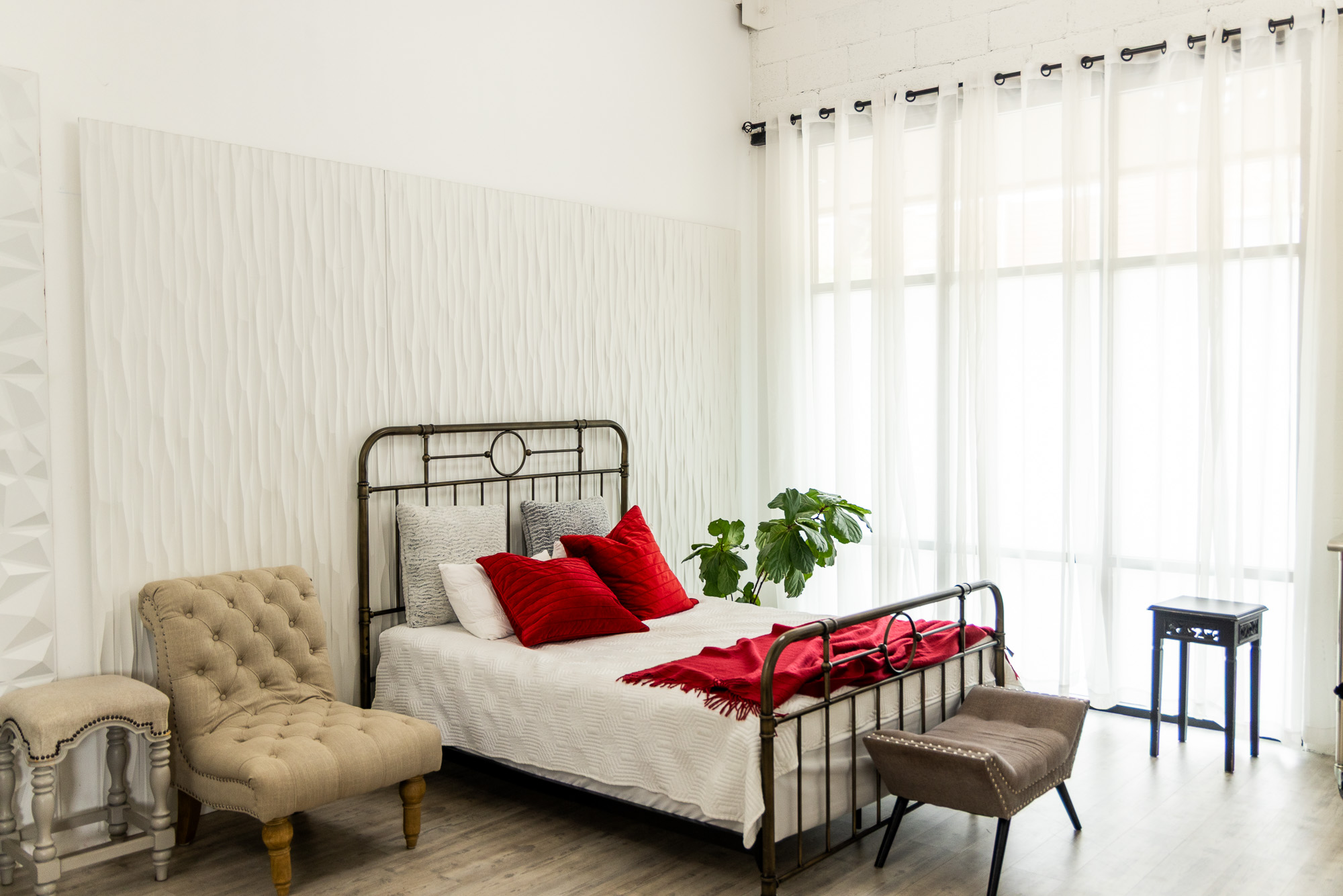 Bright studio set with an iron bed frame beside floor-to-ceiling sheer curtains