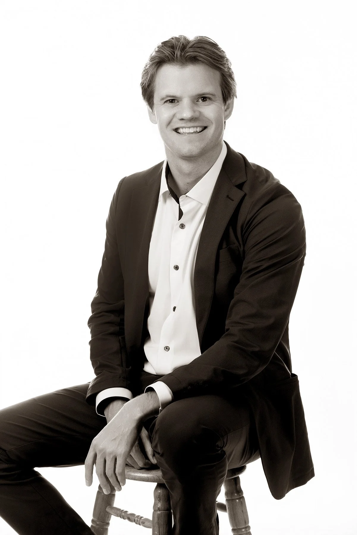 Sepia seated portrait of a man in a dark blazer on a stool