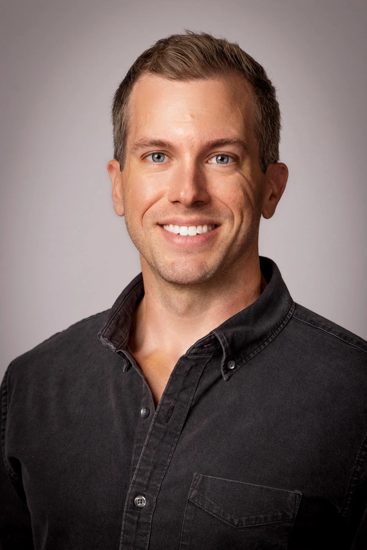 Man in a black button-down shirt on a warm grey backdrop