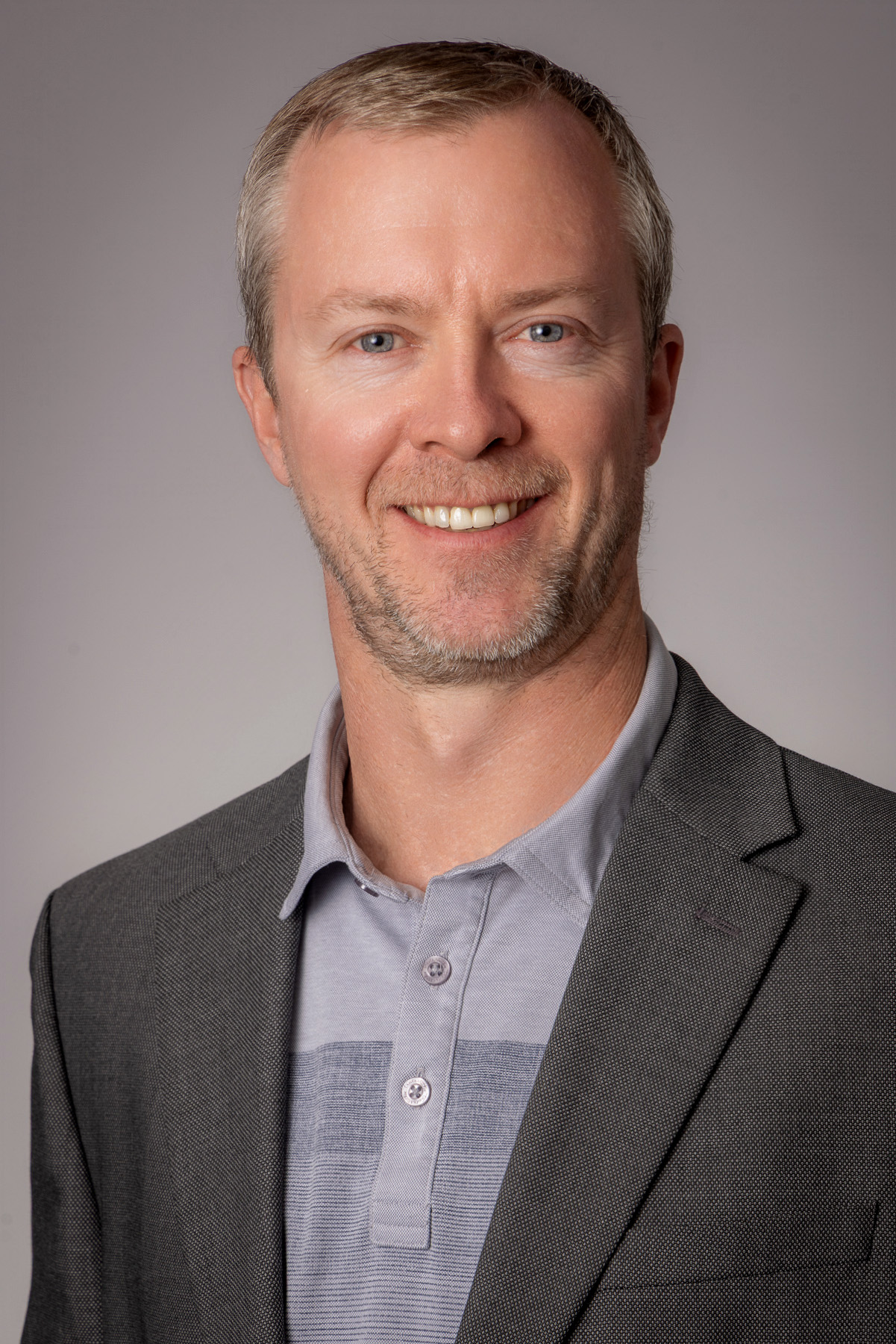 Executive in a grey blazer and lavender polo on a soft grey backdrop