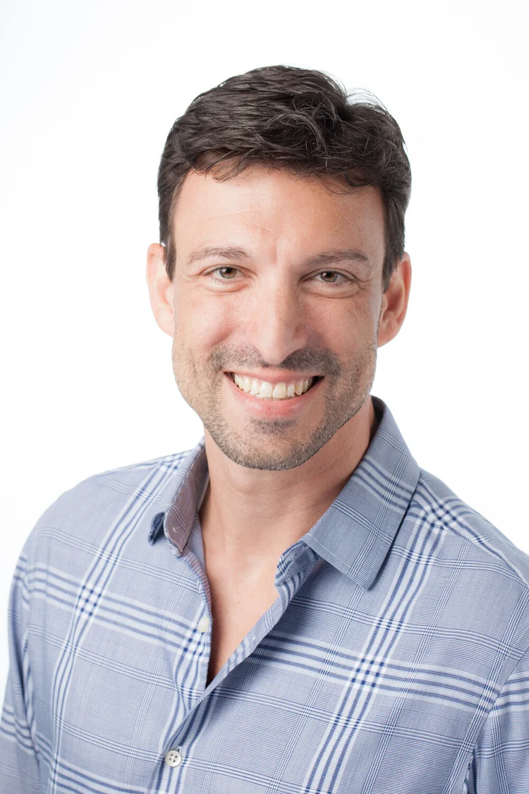 Man in a blue checked shirt smiling on a white backdrop