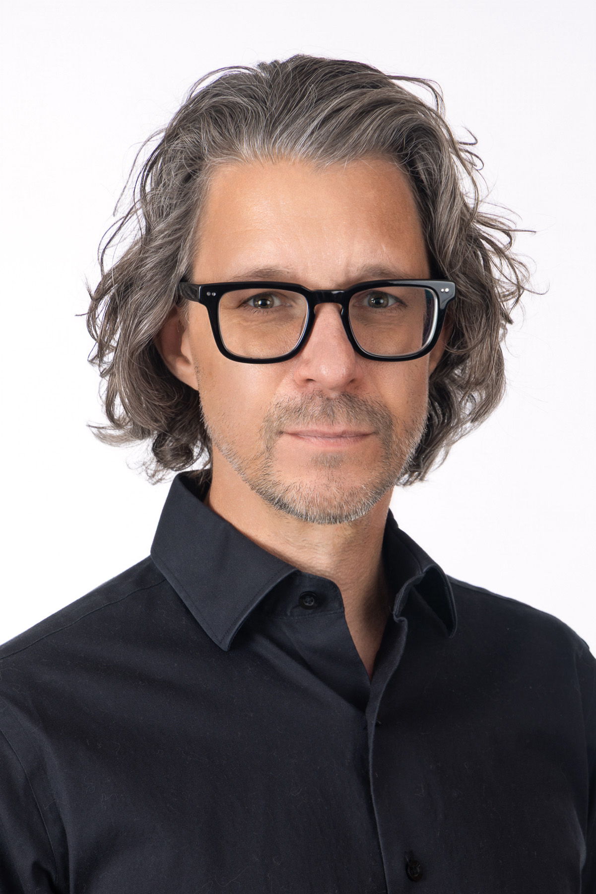 Creative director with wavy grey hair, glasses and a black shirt on white